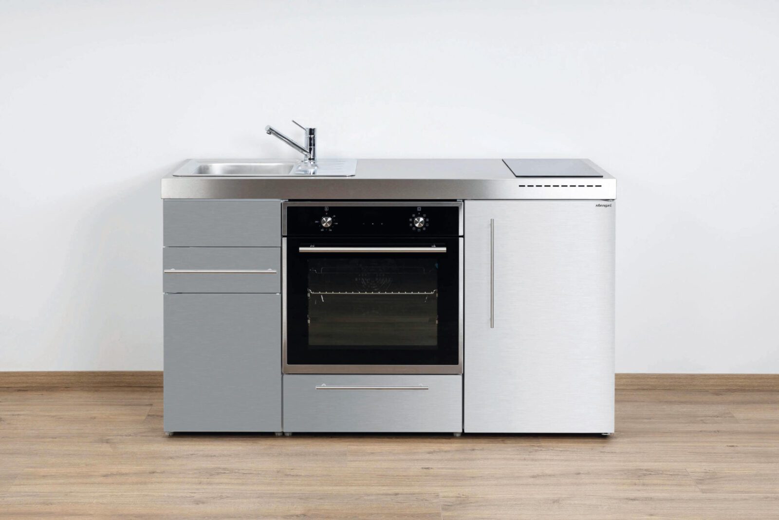 kitchenatwork Een modern roestvrijstalen keukenblok met een spoelbak, elektrische kookplaat, oven en opbergladen/kasten siert deze strakke keuken, afgezet tegen een effen witte muur en houten vloer.