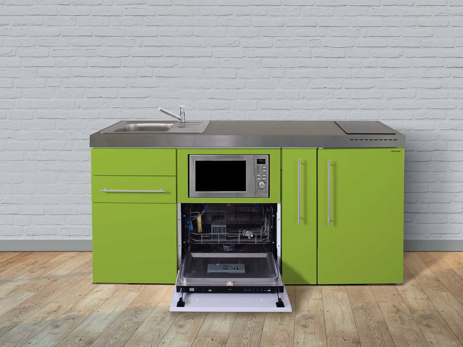 kitchenatwork Een compact groen keukenblok met RVS aanrechtblad, ingebouwde spoelbak en geïntegreerde magnetron, geplaatst boven een open vaatwasser. De unit staat tegen een witte bakstenen muur op een houten vloer.