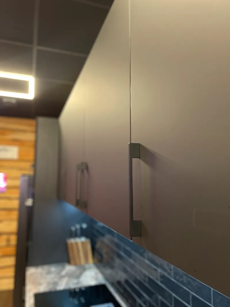 Een nijkerkkeuken met grijze kasten en een zwart aanrechtblad.