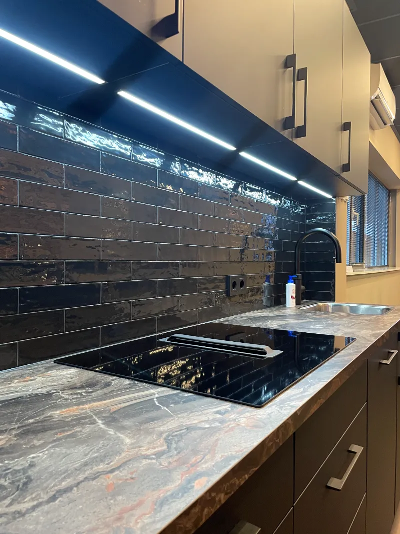 Een keuken op het werk met een zwart betegelde achterwand en een fornuis.