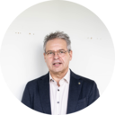 Een man met een bril en een colbert staat tegen een effen witte achtergrond. - kitchen at work